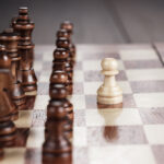 A single white wooden pawn before a group of brown chess pieces