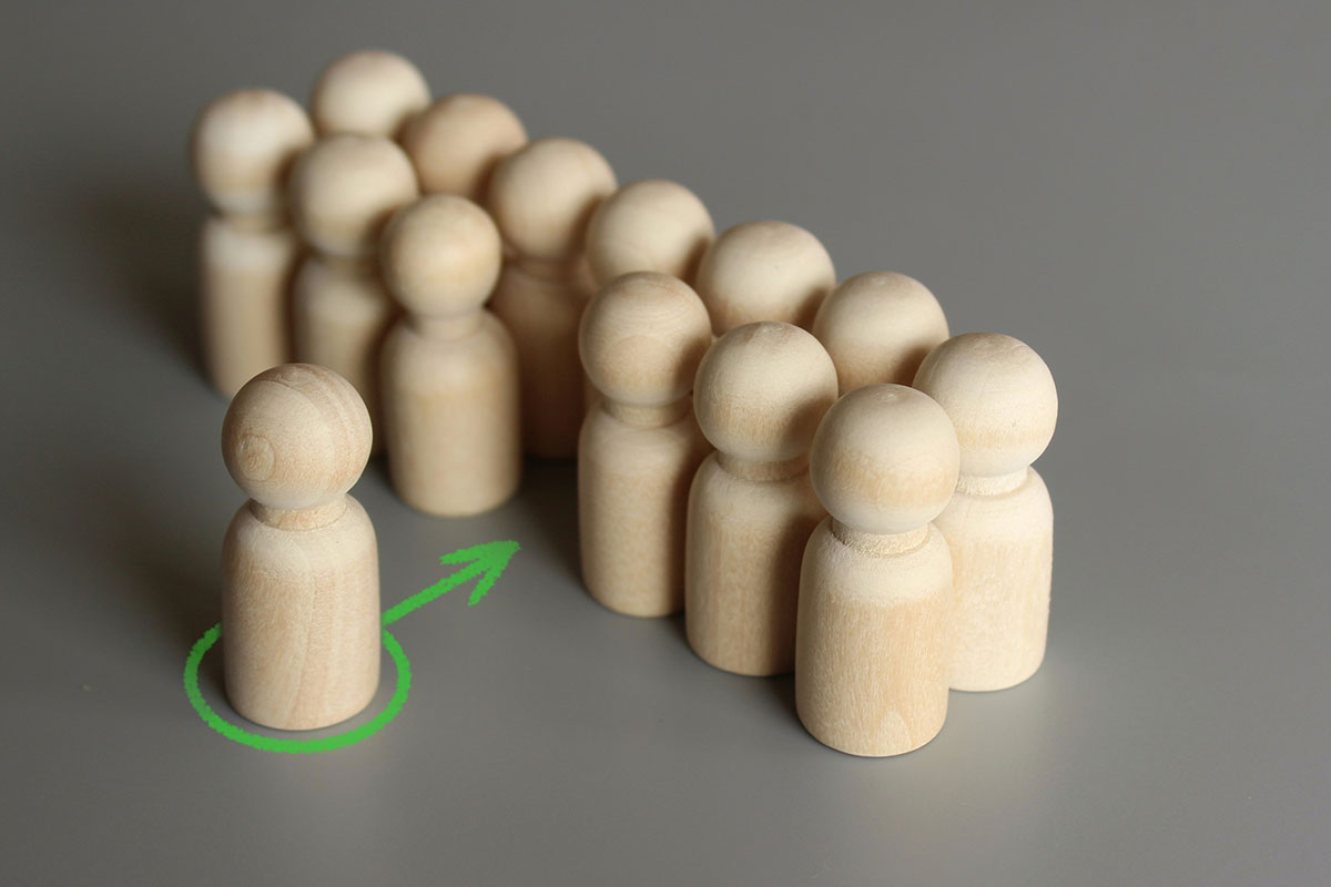 A wooden figure being accepted into a group of other wooden figures, denoted by a green arrow