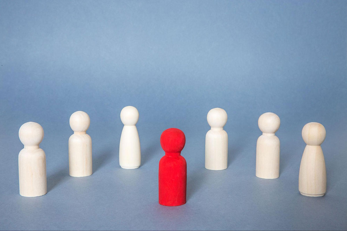 A single red wooden figure among six white figures