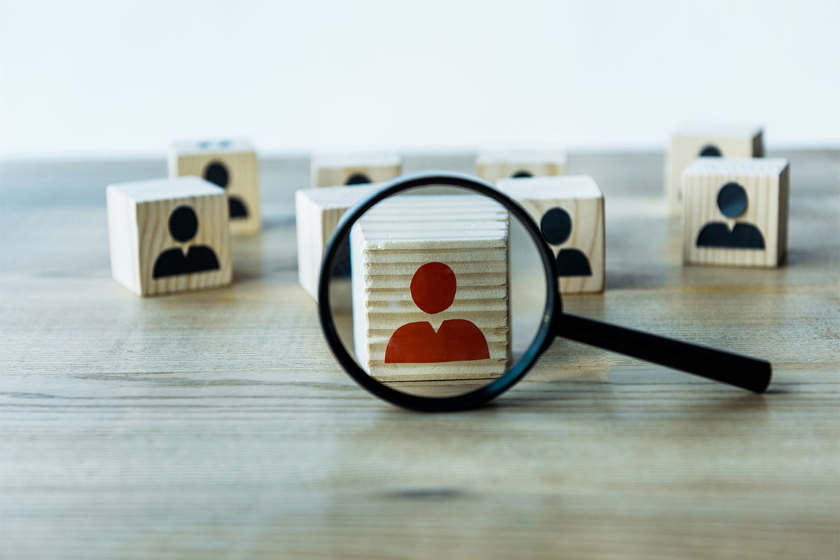 Wooden blocks on a table depicting people as one of the figures is examined through a magnifying glass
