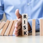 A man holds dominos back from toppling down blocks that spell RISK